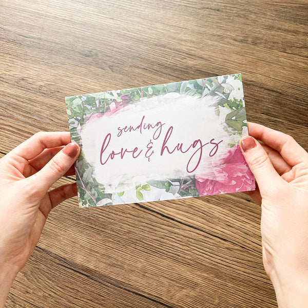 hands holding floral card that says sending love and hugs