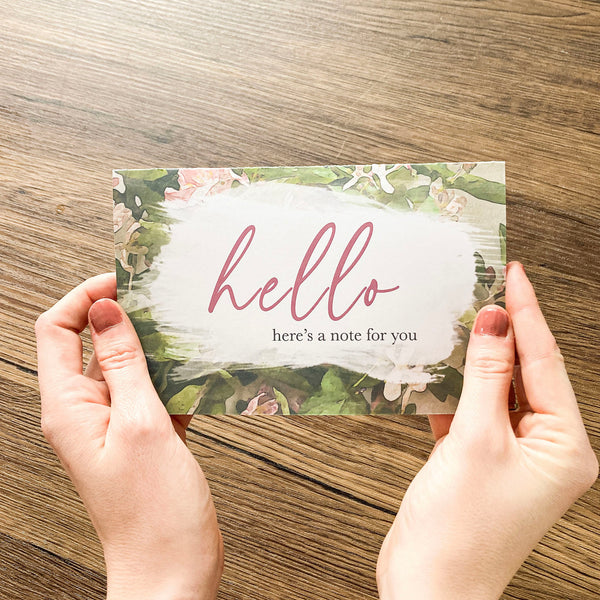 hands holding floral card that says hello, here's a note for you